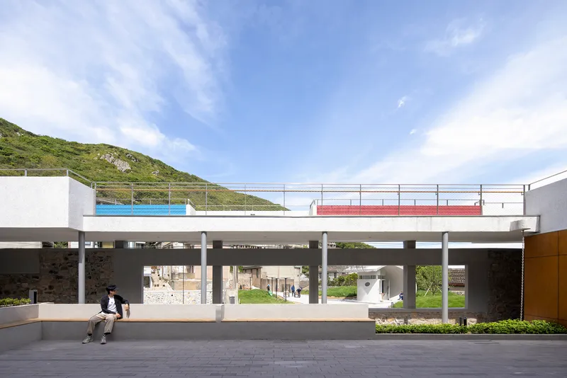 Elevated concrete platform on columns with colored panels and two people seated below