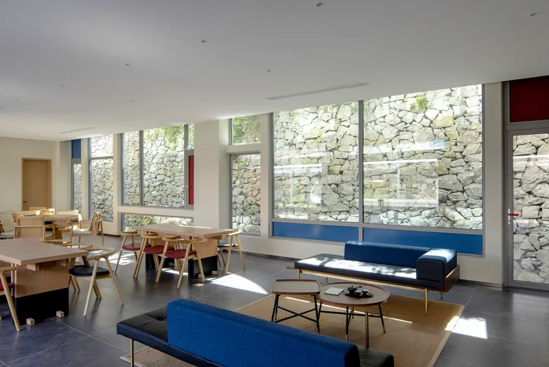 Interior space with floor-to-ceiling windows framing a stone wall and sunlight streaming across the floor
