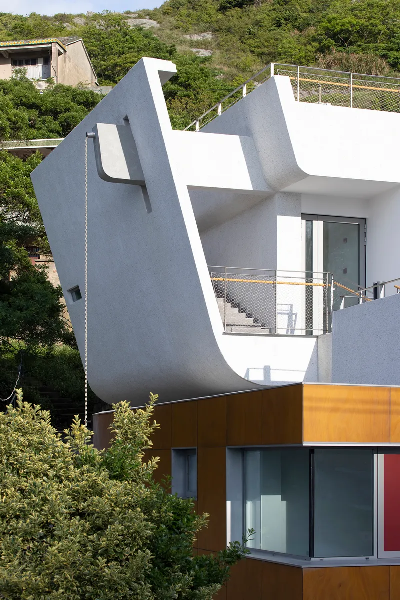 Angled white facade with metal railings and mustard-colored lower volume set against dense hillside vegetation
