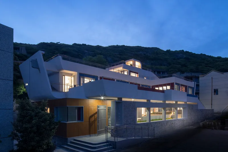 Exterior view of the white terraced facade with curved roofline illuminated at dusk against a forested hillside