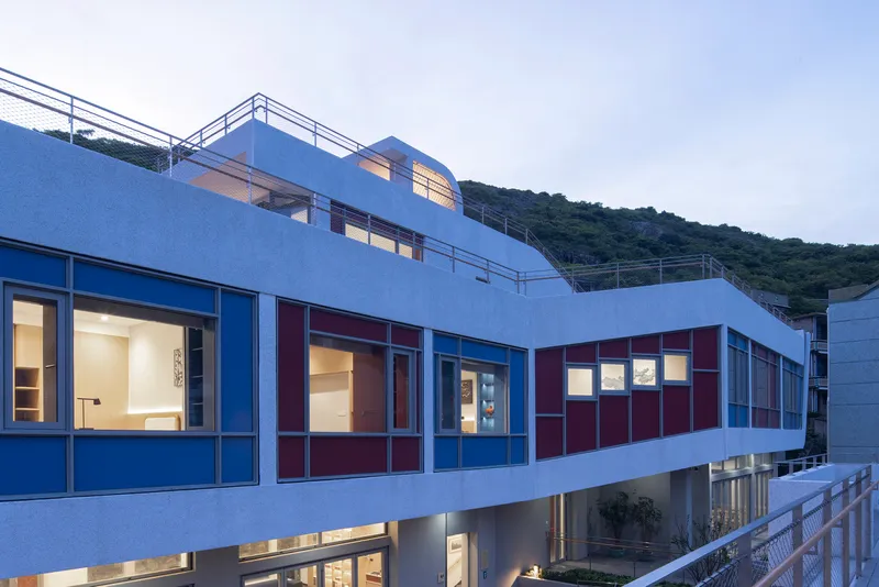Upper terrace and facade showing blue and maroon panels with stepped roof volumes at twilight