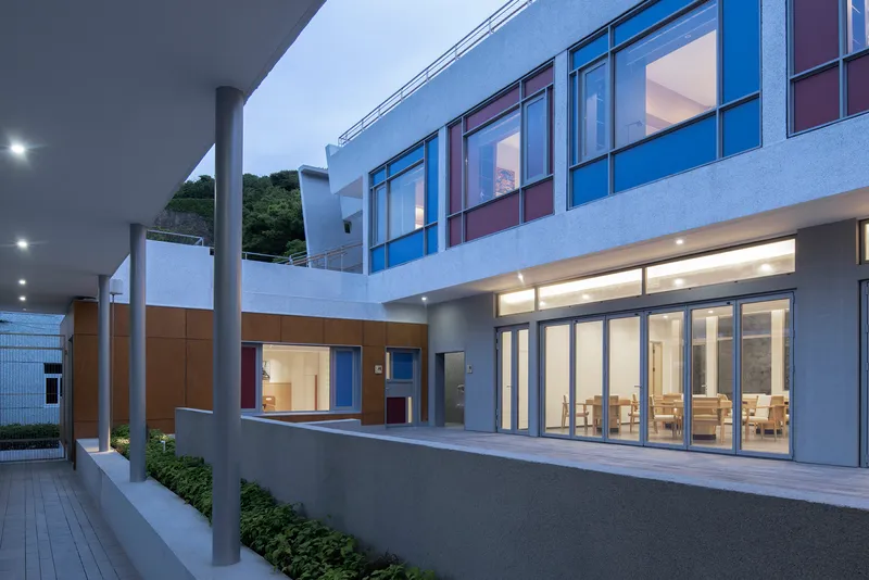 Courtyard view at dusk with ground-floor dining hall glazing and cantilevered columns along the entry drive