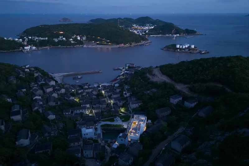 Drone view of illuminated rooftop among coastal village buildings at twilight