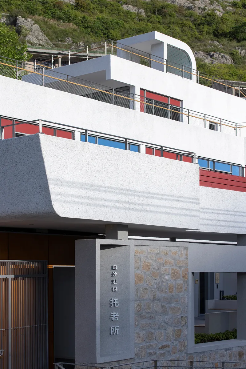 Entry gate with stone wall and signage below white terraced levels with colored window panels