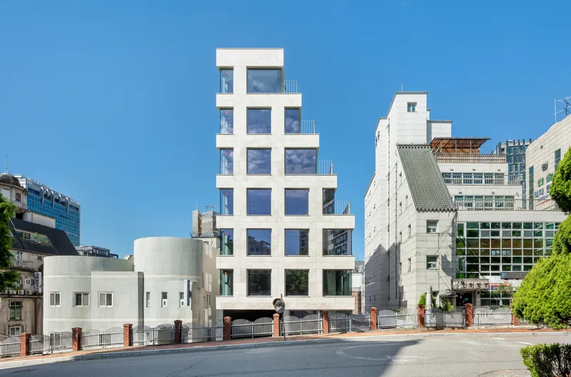 Street view of the white stepped facade rising between existing buildings on a clear day