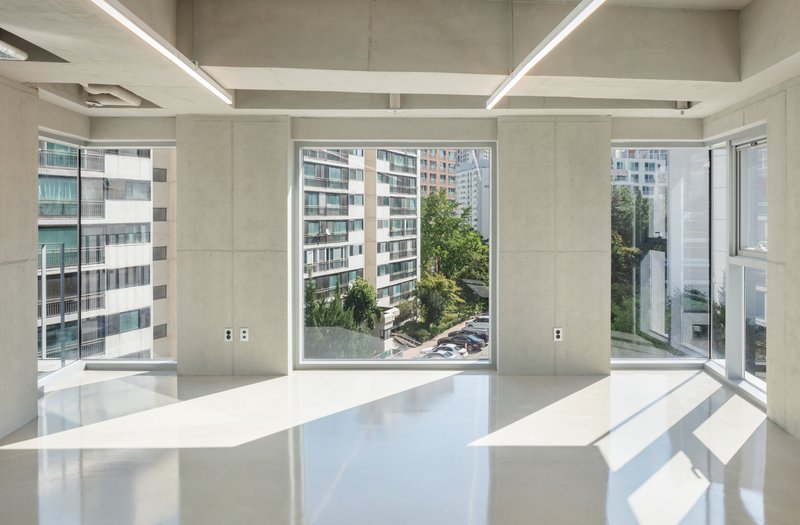Interior space with exposed concrete ceiling beams and floor-to-ceiling windows overlooking neighboring buildings