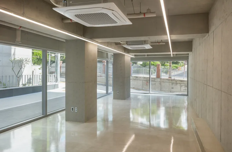 Open floor space with exposed concrete columns, linear light fixtures, and glazed storefronts along the street