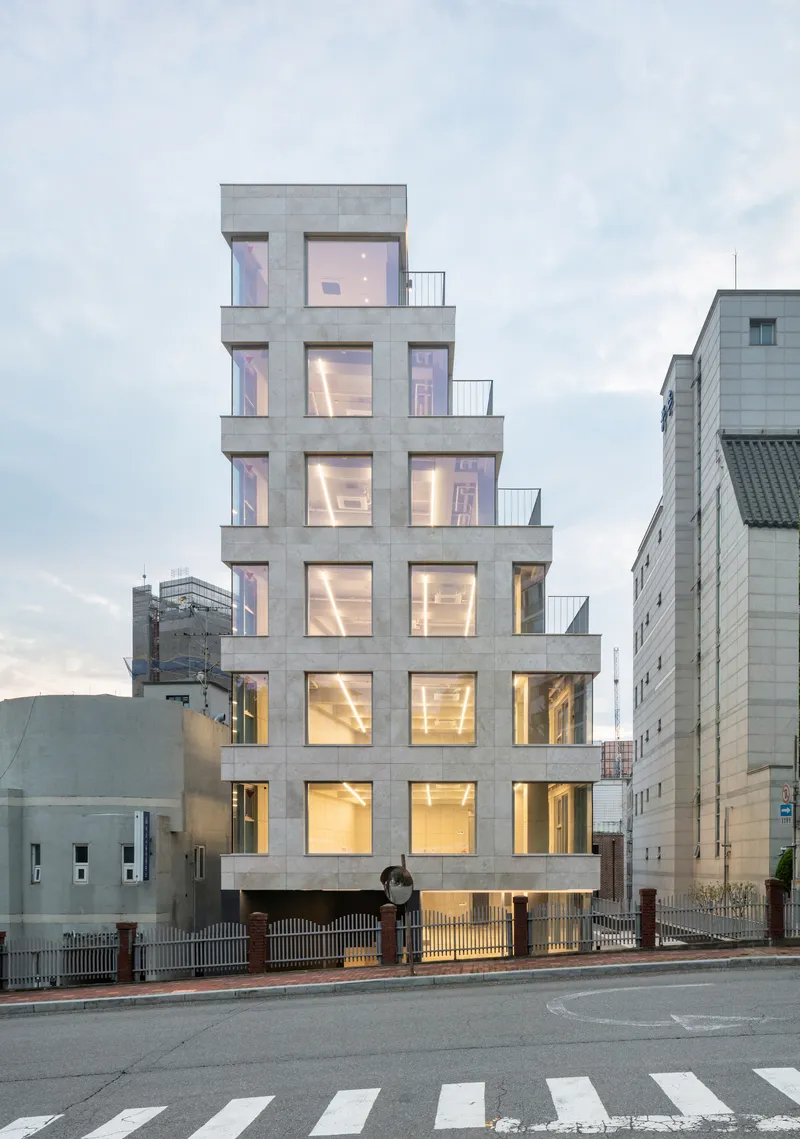 Street view of the stepped concrete facade with illuminated interiors at dusk