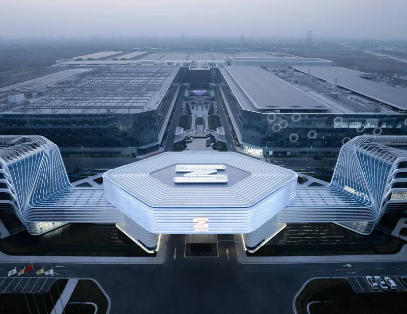 Aerial view of the hexagonal central canopy flanked by curved ribbed pavilions and linear exhibition halls in hazy daylight