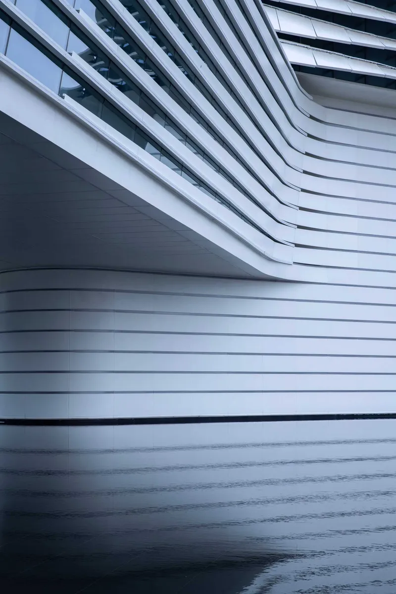 Close-up of the horizontal metal fins curving across the facade with wet pavement reflecting below