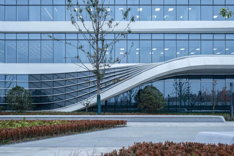 Curved pedestrian bridge spanning a landscaped courtyard with planted beds and young trees
