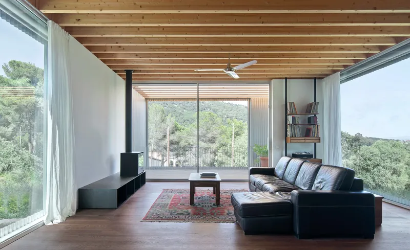 Living room with exposed timber ceiling joists and floor-to-ceiling glazing overlooking wooded hillside