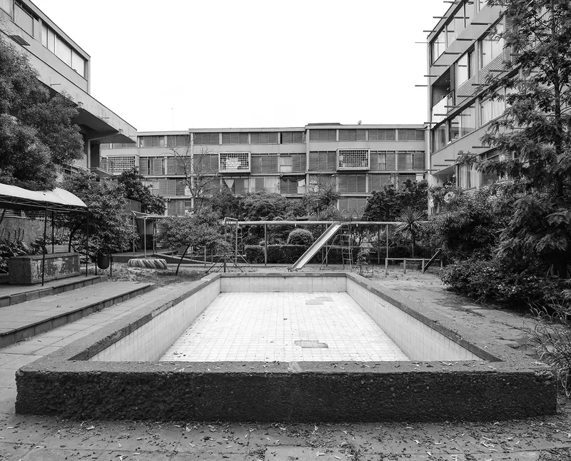 Drained swimming pool in a courtyard garden surrounded by three-story residential blocks and trees