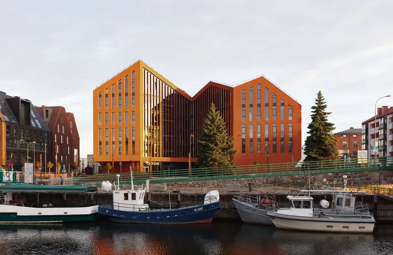 Harborside view of the three connected volumes at dusk with boats docked along the quay