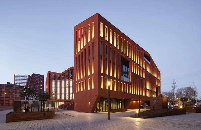 Corner view at dusk showing interior lighting through the vertical terracotta louvers and courtyard planters