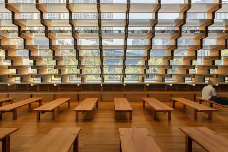 Interior reading room with horizontal timber bookshelves and a lone reader at a low bench table