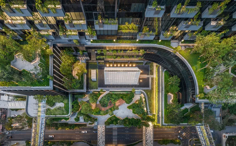 Aerial view of curved vehicular drive threading through planted roof terraces at dusk with lights on