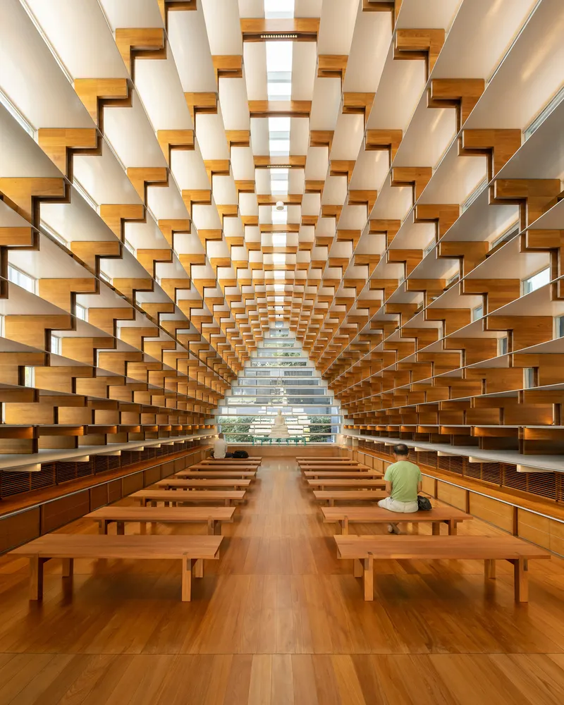 Interior view of the timber shelf-lined hall with wooden benches and a seated visitor in green