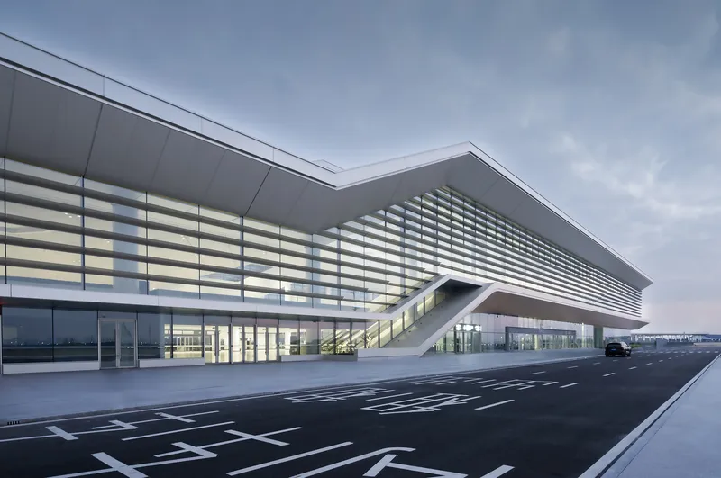 Cantilevered entrance canopy with horizontal louvers above glass walls and freshly paved roadway at dusk