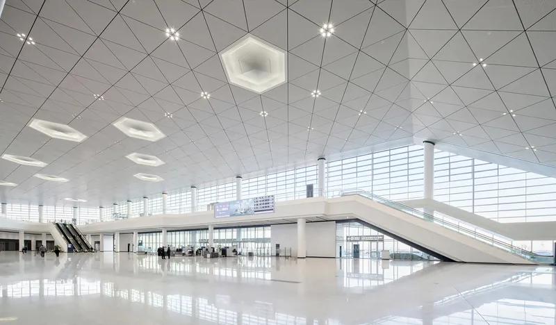 Interior departure hall with white polished floor, triangular ceiling panels and hexagonal skylights
