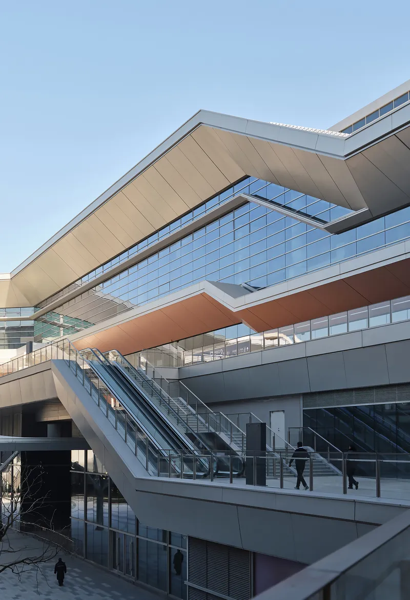 Stacked horizontal volumes with glazed facades and outdoor escalators carrying passengers between levels