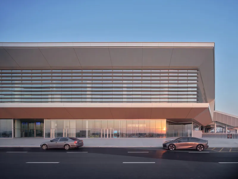 Curbside drop-off zone with horizontal louvers above glass wall and two cars in motion