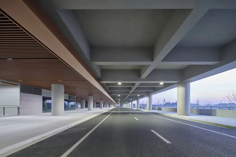 Covered roadway with concrete beams and cylindrical columns framing an open horizon at dusk