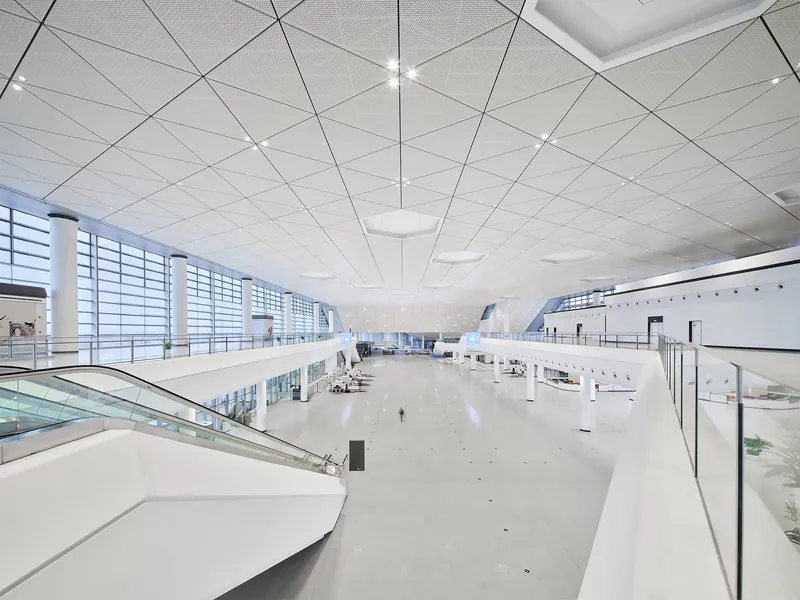 Interior departure hall with perforated white ceiling panels and glass curtain wall overlooking the tarmac