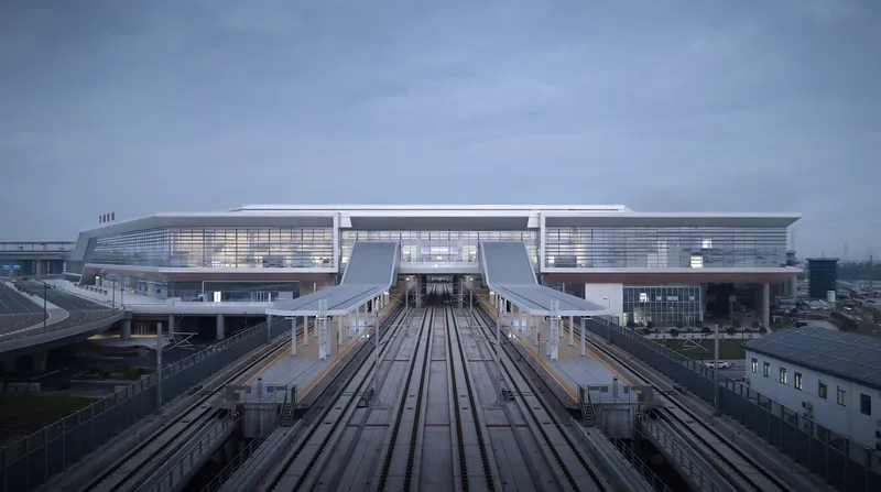 View along elevated rail tracks leading to the illuminated terminal building under overcast skies