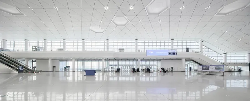 Interior departure hall with white tile ceiling, mezzanine level and passengers near service counters