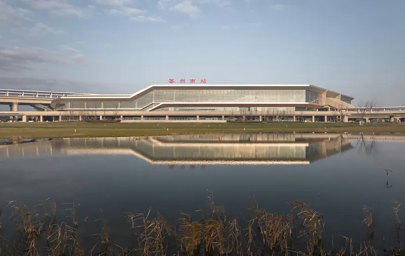 Long horizontal terminal building with banded facade reflected in a still pond with dried reeds