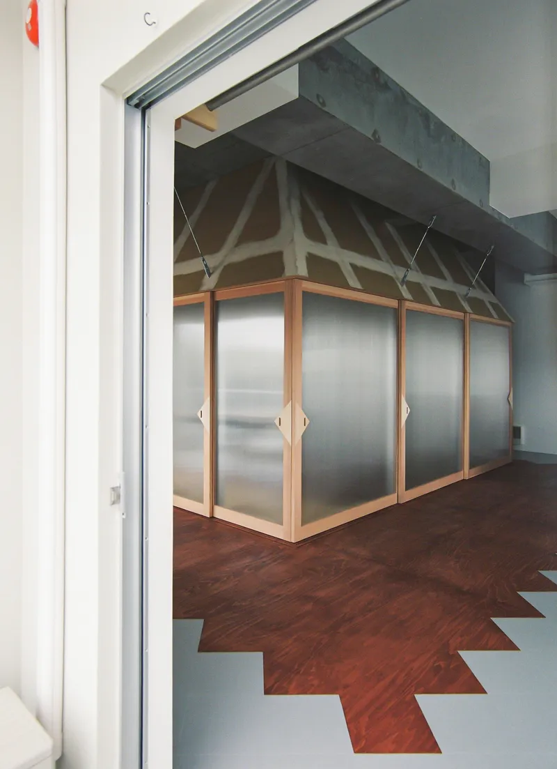 Timber-framed translucent partition wall with exposed truss structure visible above and chevron floor pattern