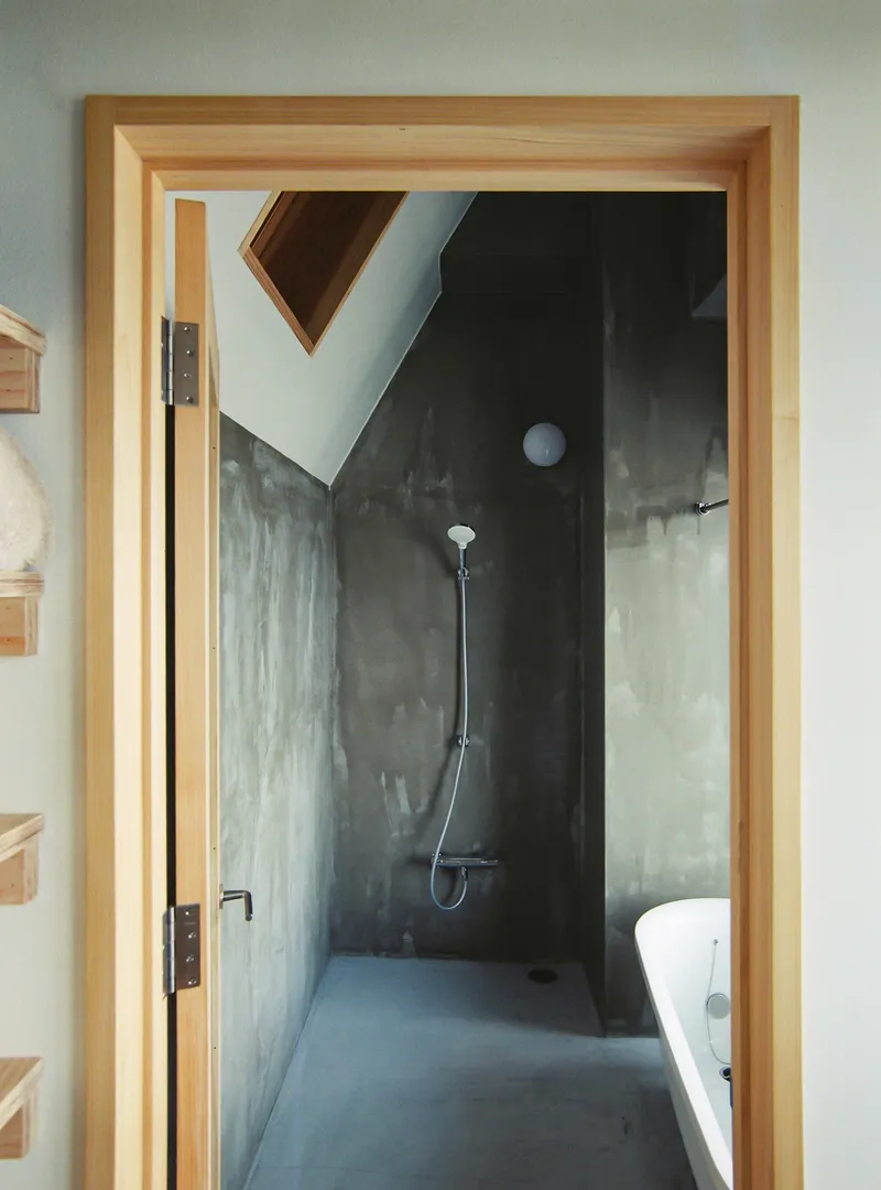 Bathroom with polished concrete walls, timber-framed doorway, wall-mounted shower and angled skylight overhead