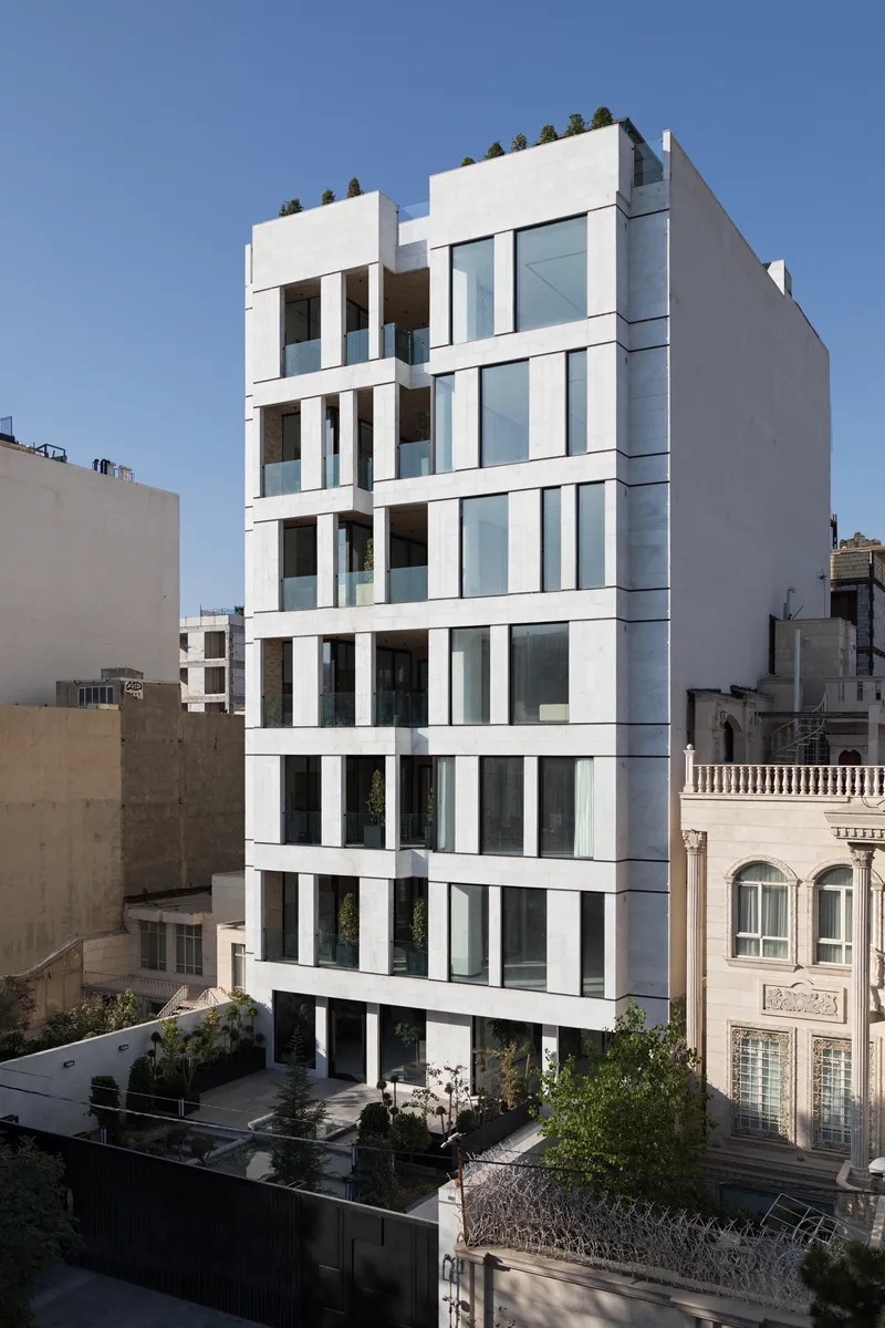 White facade with recessed balconies and floor-to-ceiling glazing among neighboring residential buildings