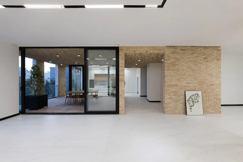 Open plan interior showing textured brick volumes dividing spaces with pale stone floor and glazed terrace beyond