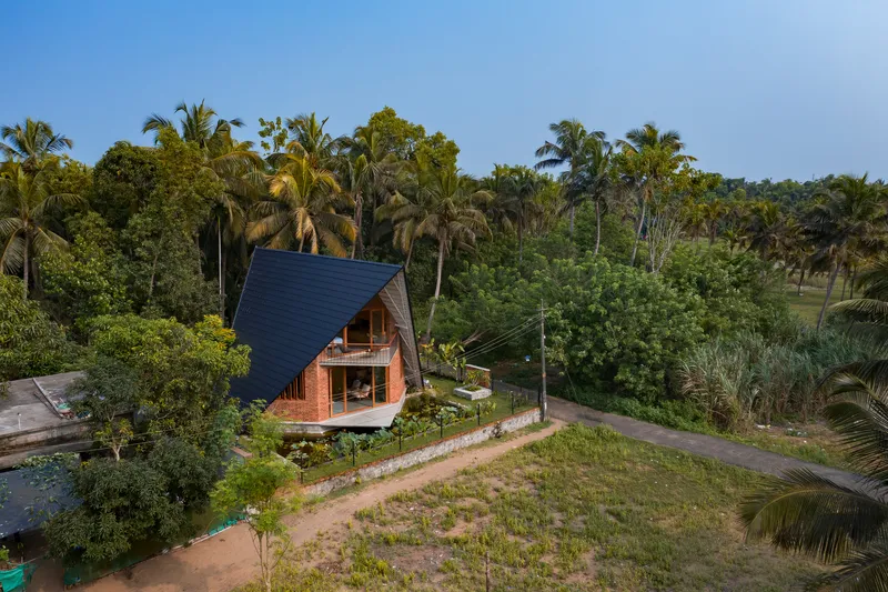 Aerial view of the A-frame brick residence with steep dark tiled roof amid dense tropical palms