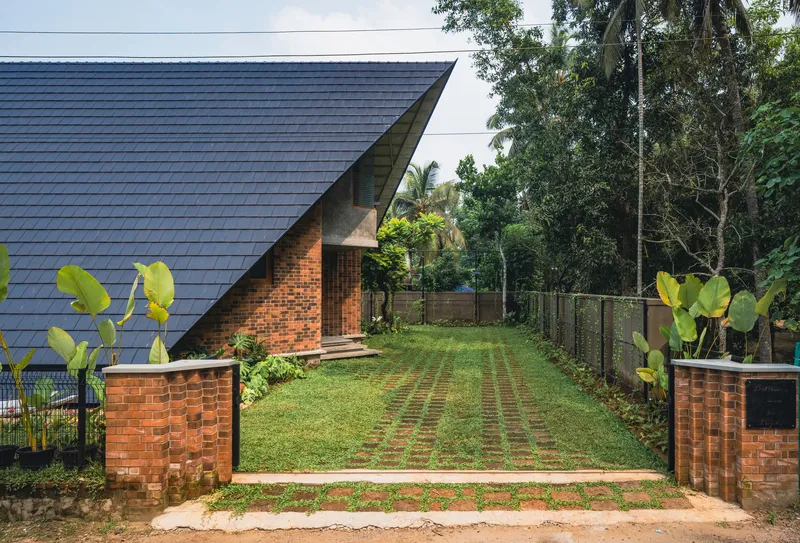 Entry driveway with grass pavers and perforated brick gateposts leading to the dark tiled roof volume