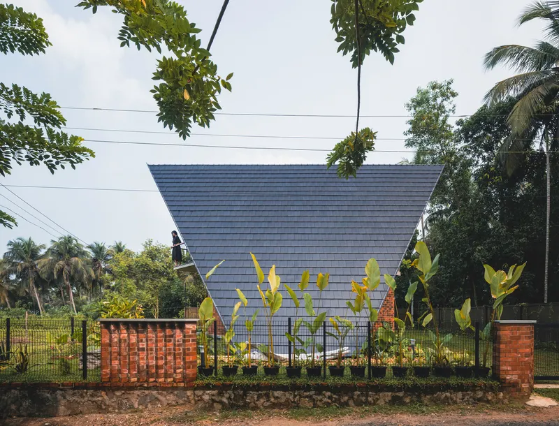 Side view of the tilted gable roof and perforated brick screen walls with young banana plants along the fence