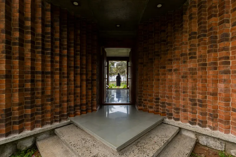 Covered entry corridor with perforated brick walls and polished concrete floor looking toward glazed doorway and garden