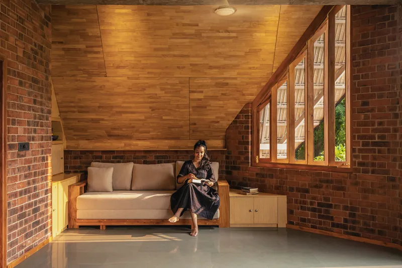 Living area with wood plank ceiling, brick walls, and woman seated reading on a sofa