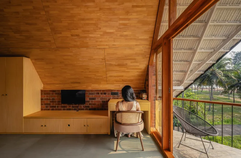 Mezzanine workspace with timber ceiling vault and metal railing overlooking palm trees through the slanted glass wall