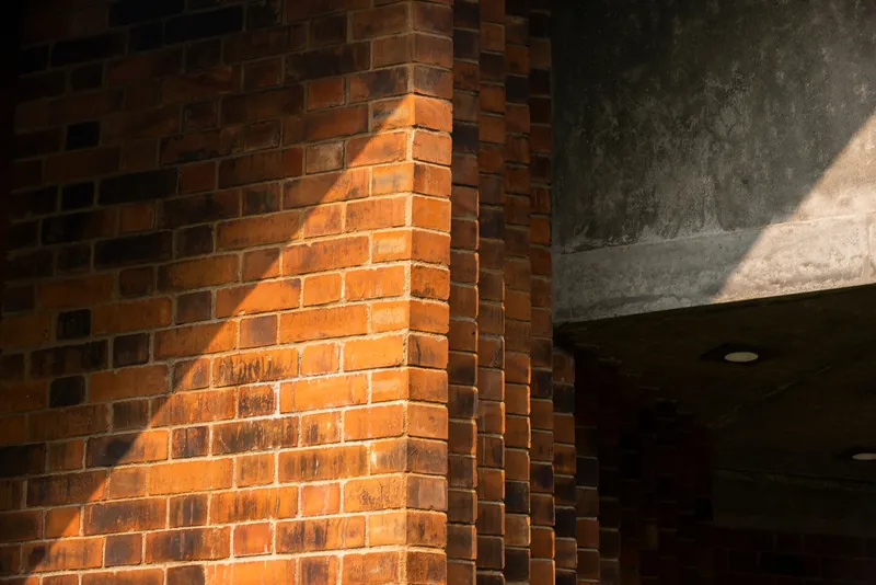 Corner detail of red brick wall meeting the concrete ceiling in afternoon sunlight