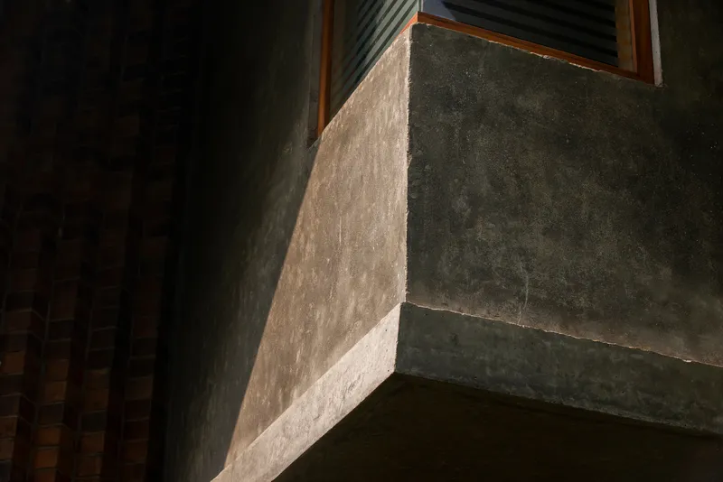 Concrete beam edge and window opening catching raking light across the textured plaster surface