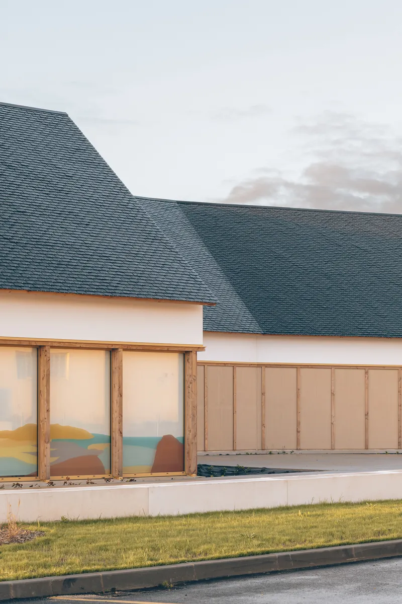 Detail of the dark slate roof meeting white walls and timber-framed glazing with lawn in foreground