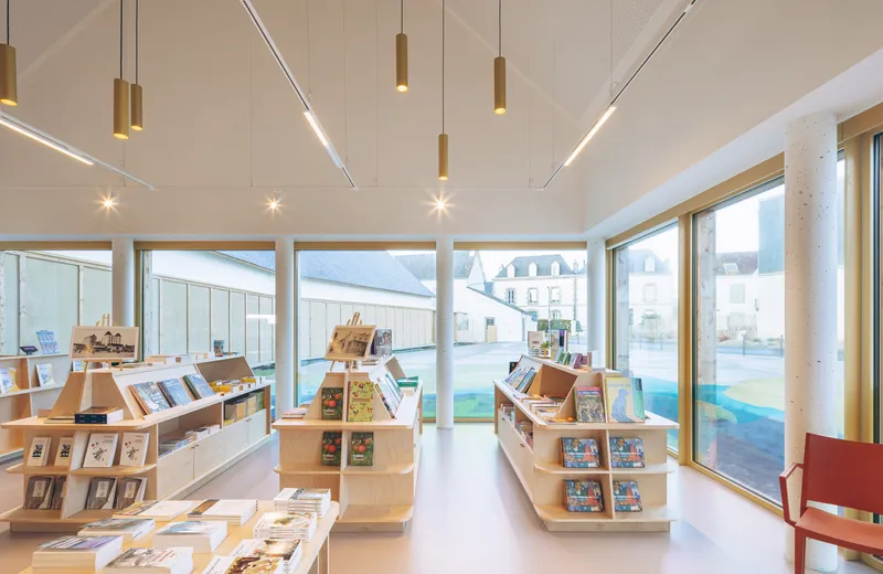 Interior retail space with plywood display shelves beneath linear lighting and timber-framed windows
