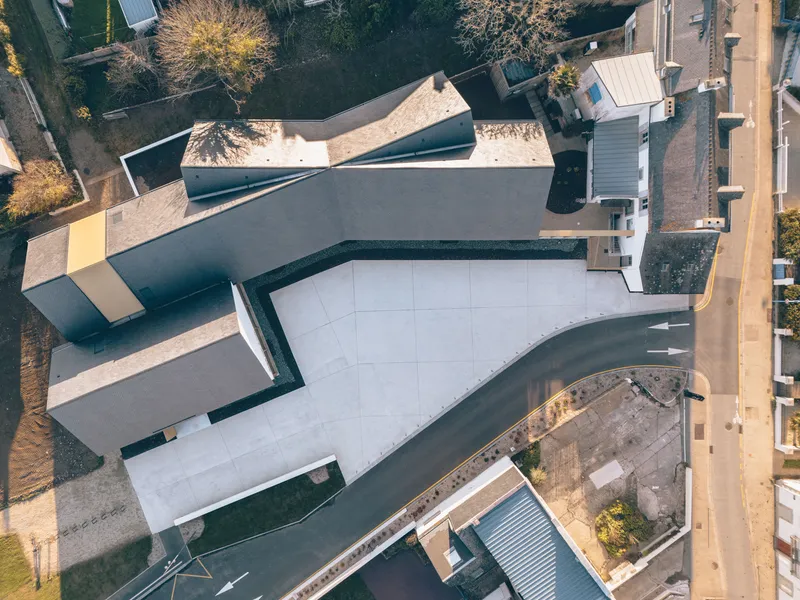 Overhead view showing curved white courtyard surface bordered by angular dark zinc rooflines and adjacent rooftops