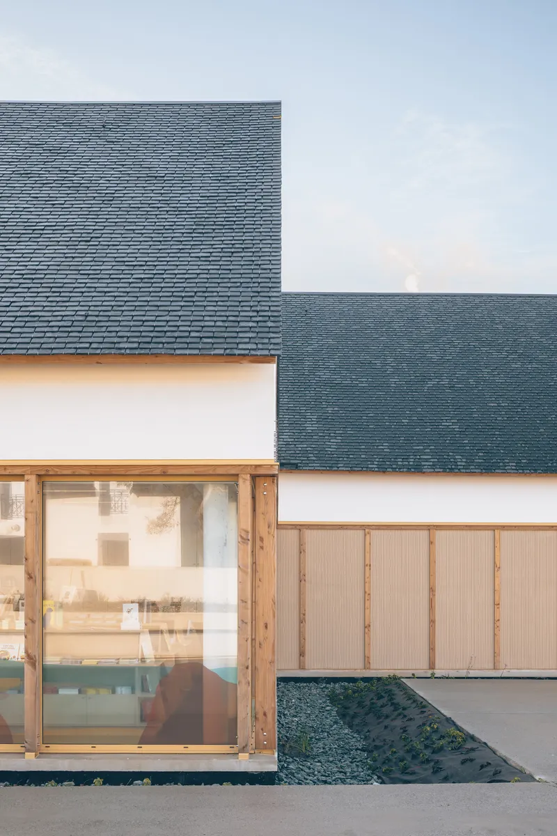 Close-up of intersecting gabled rooflines with dark slate tiles above timber-framed glazing and gravel edging