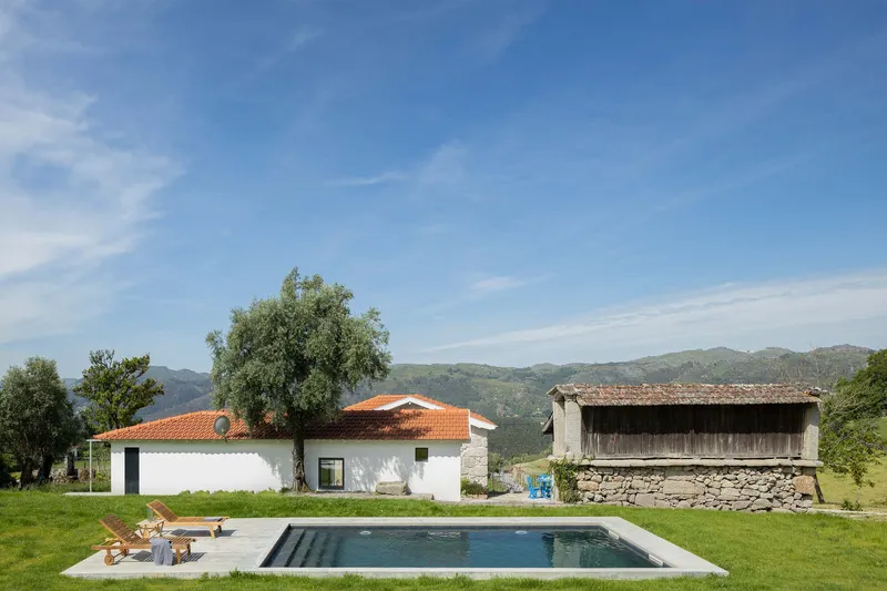Rectangular pool and whitewashed house with terracotta tile roof set against green hills under open sky