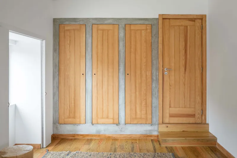Built-in wardrobe with three timber doors framed by raw concrete on a timber floor