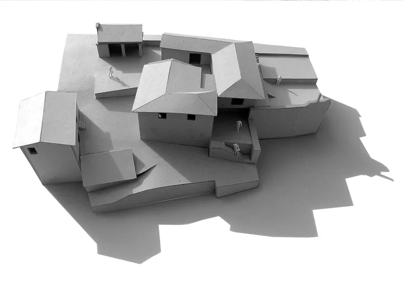 Physical model showing clustered volumes with pitched roofs and courtyards arranged across a sloped site